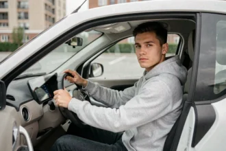 Jeune homme au volant d'une voiture sans permis dans un parking urbain, illustrant la conduite d'une VSP